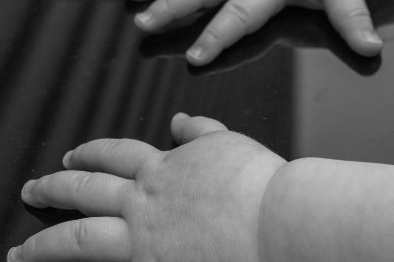 Adult hand resting alongside an infant's hands, illustrating the gentle listening touch used in visceral osteopathy