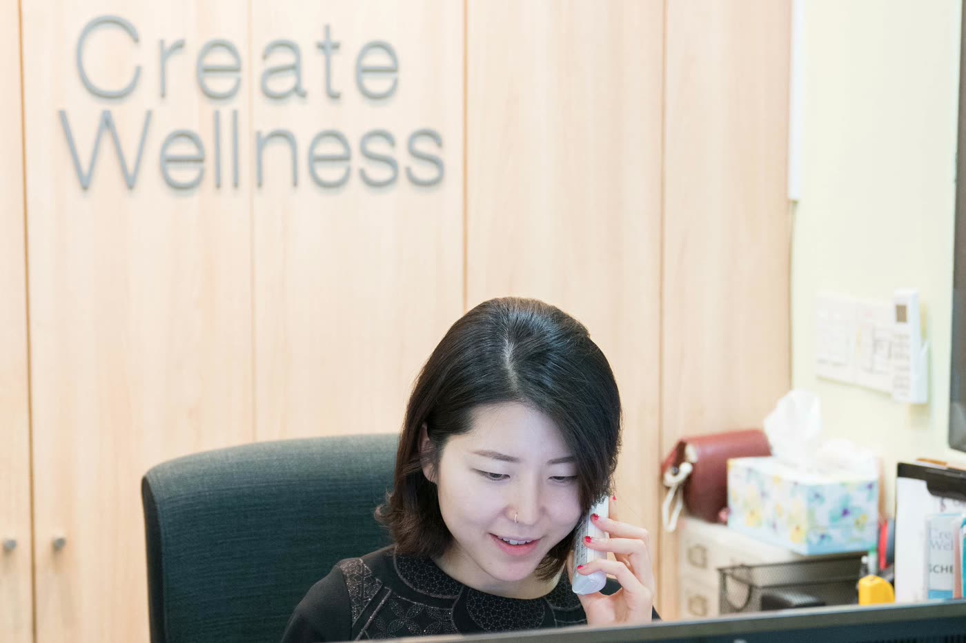Create Wellness Center receptionist taking a phone call at the front desk under the clinic's wall lettering