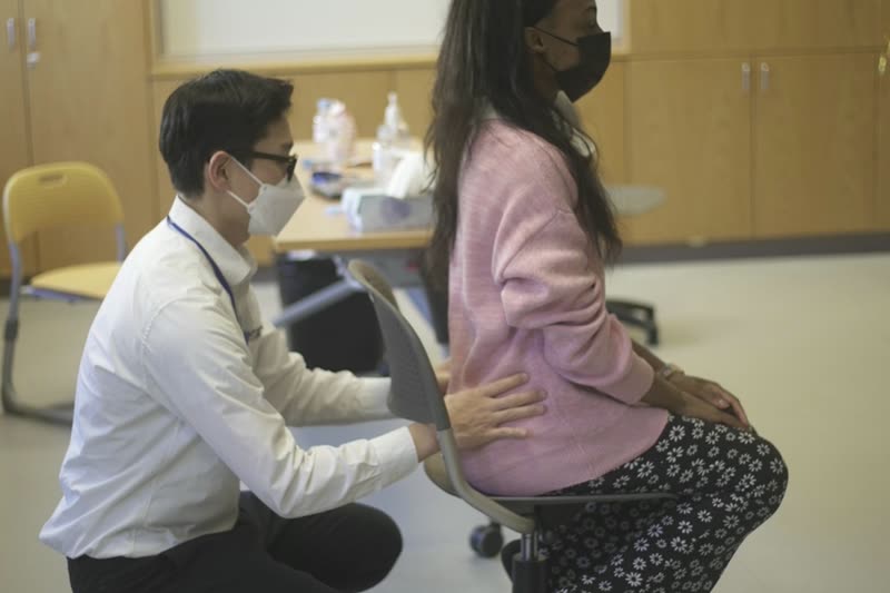 Practitioner assessing an office worker's seated posture during a workplace ergonomics assessment